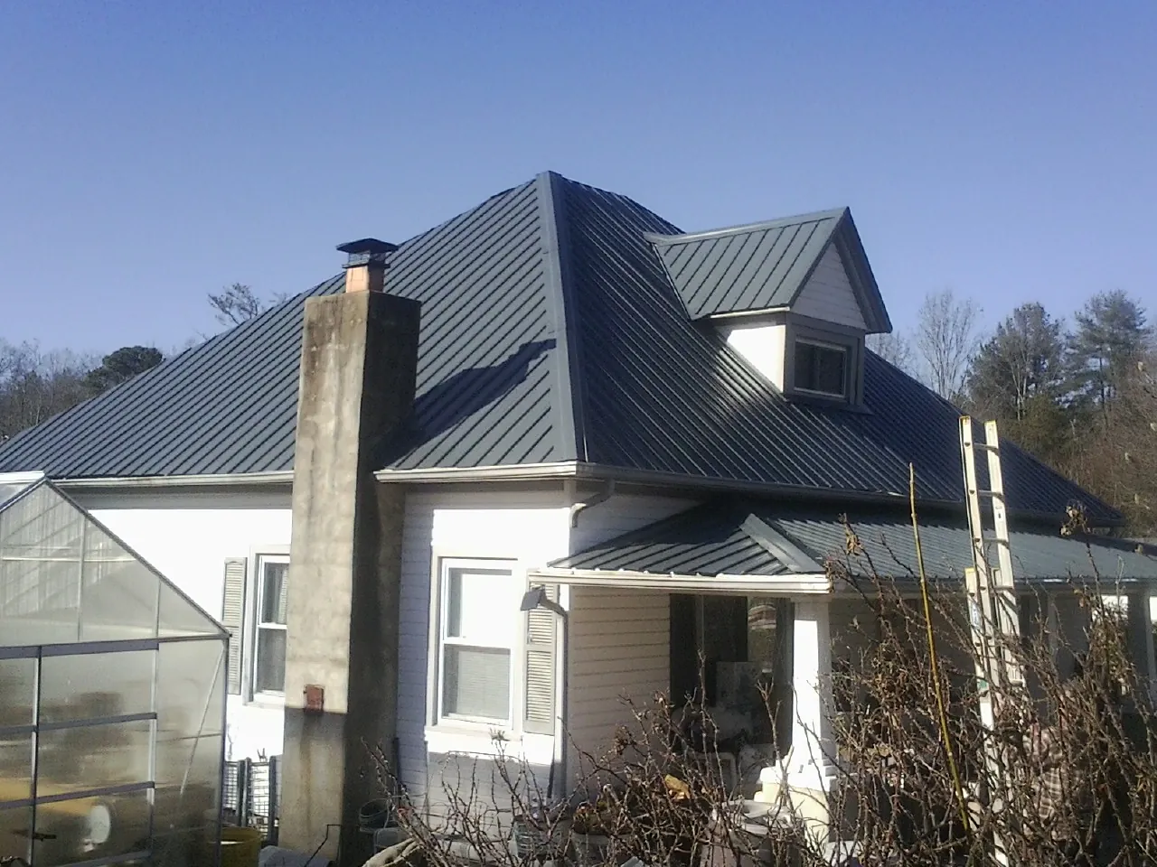 Dark blue standing seam metal roof on a white farmhouse with dormer — Slate & Tile Roof Repair by Roofing Brothers in Labadie