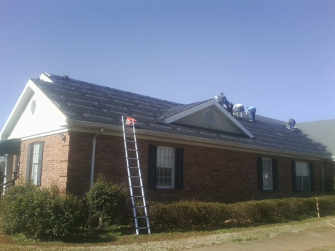 Crew tearing shingles off a brick ranch roof with a ladder set — Metal Roof Repair work by our crew in Labadie