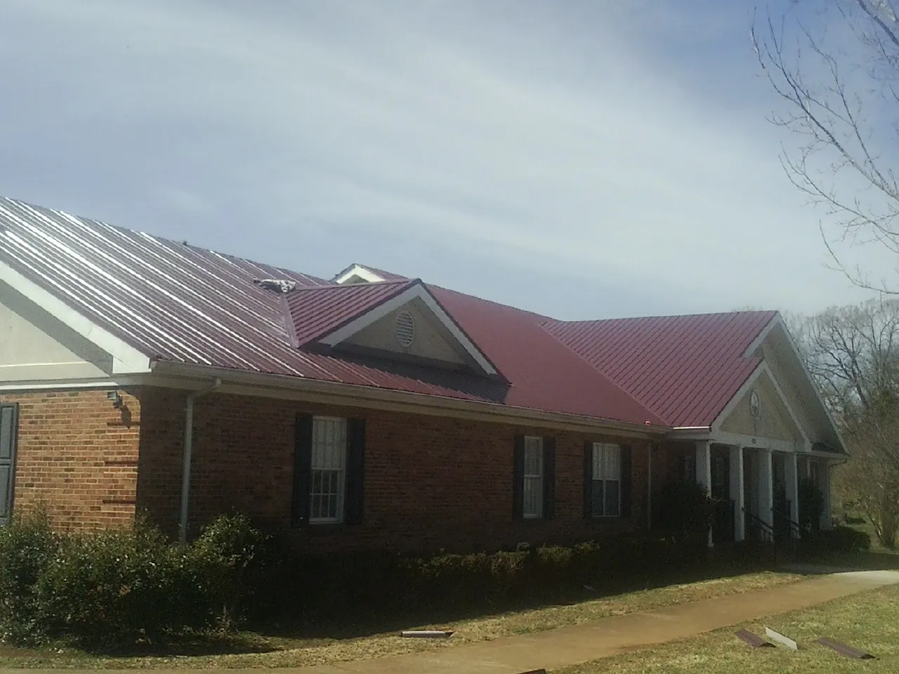 Red metal roof with gabled entries on a long brick building, from a Hail Damage Roof Repair job in Labadie