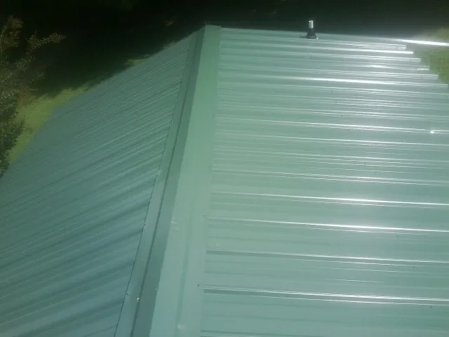 New green metal panels meeting at the ridge of a roof — Flat Roof Repair work by our crew in Labadie