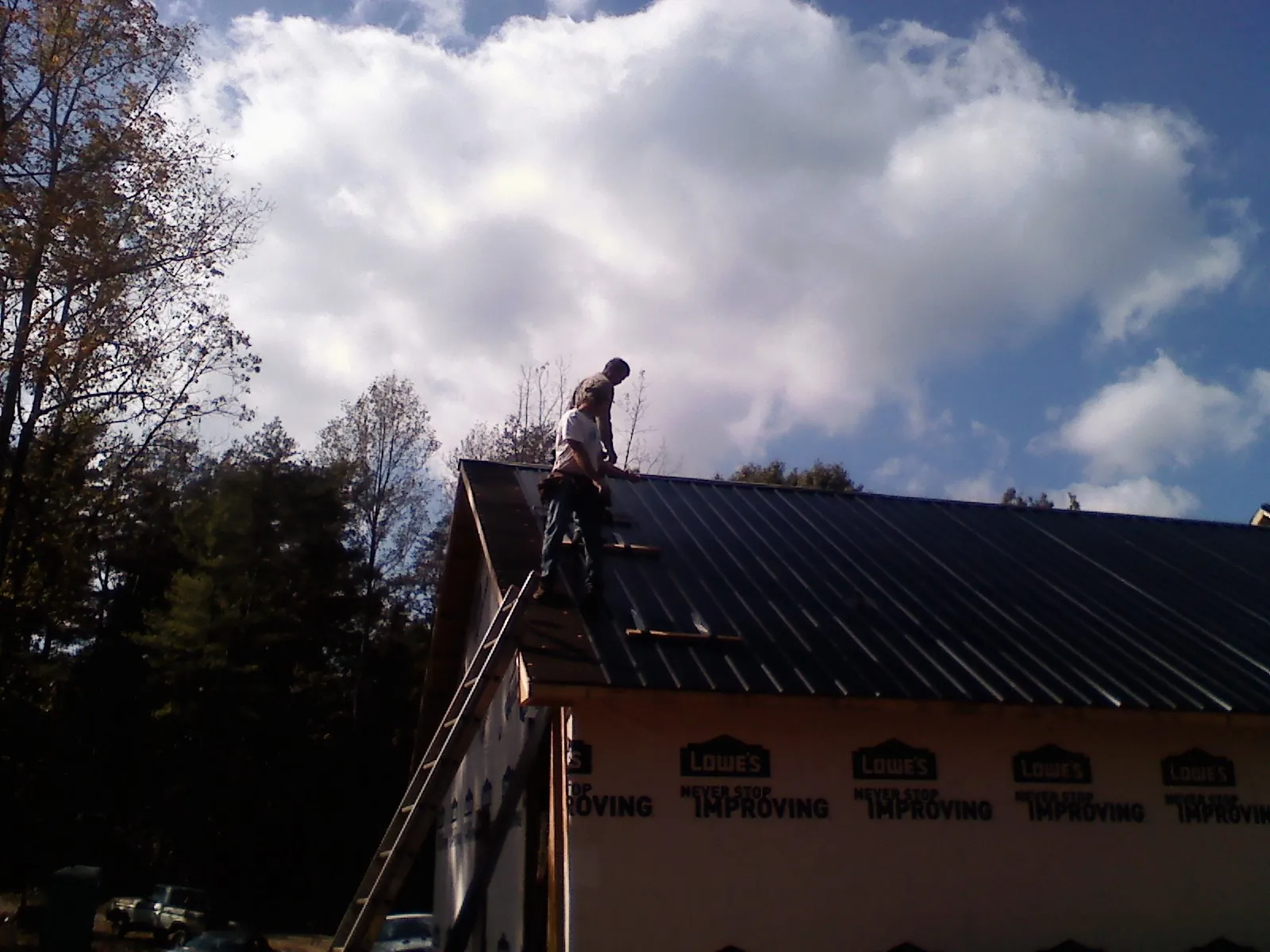 Roofer fastening dark metal panels high against a cloudy sky, from a Roof Inspection job in Labadie