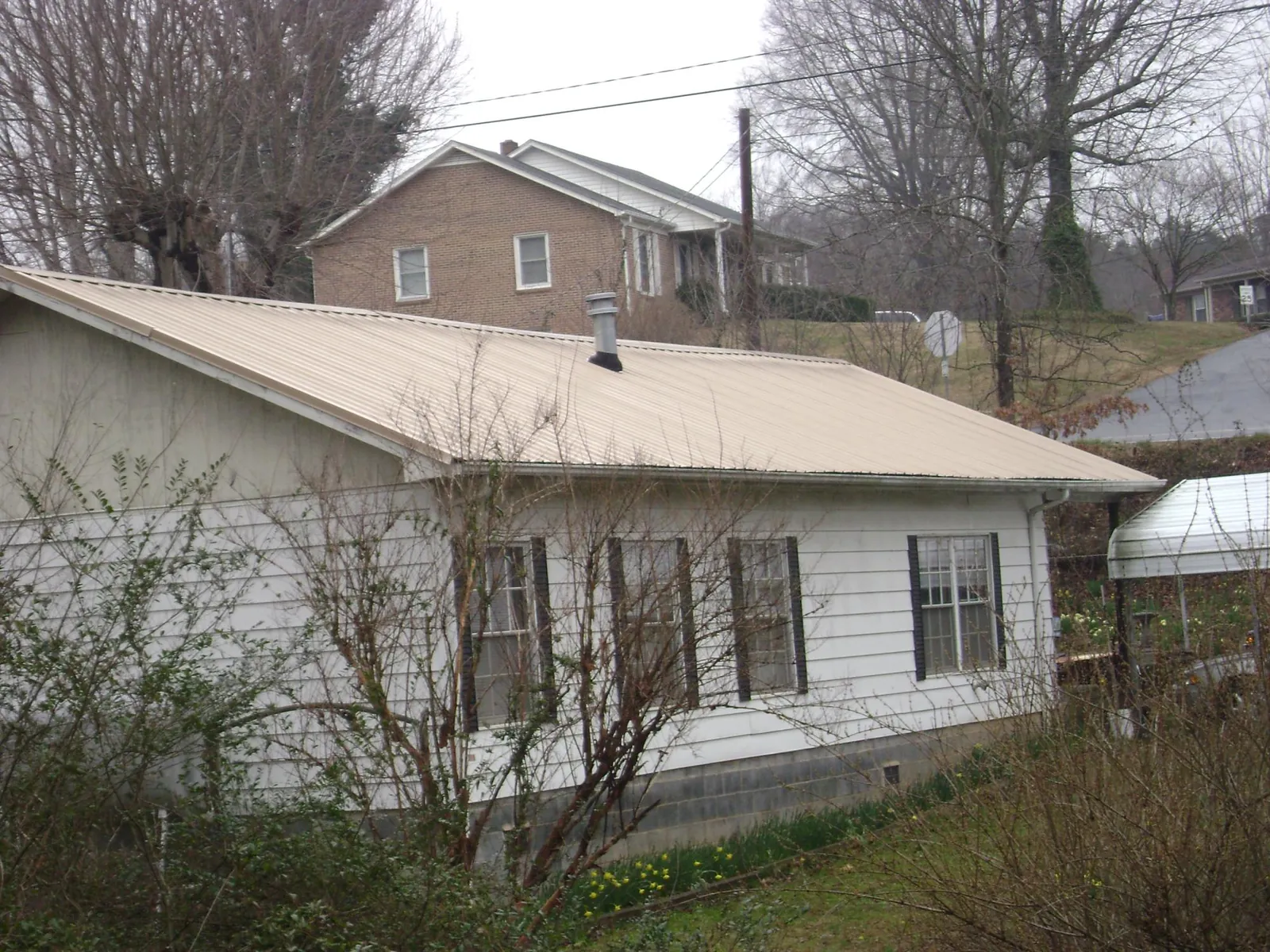 Tan metal roof on a white sided house set into a hillside — Commercial Roofing by Roofing Brothers in Labadie