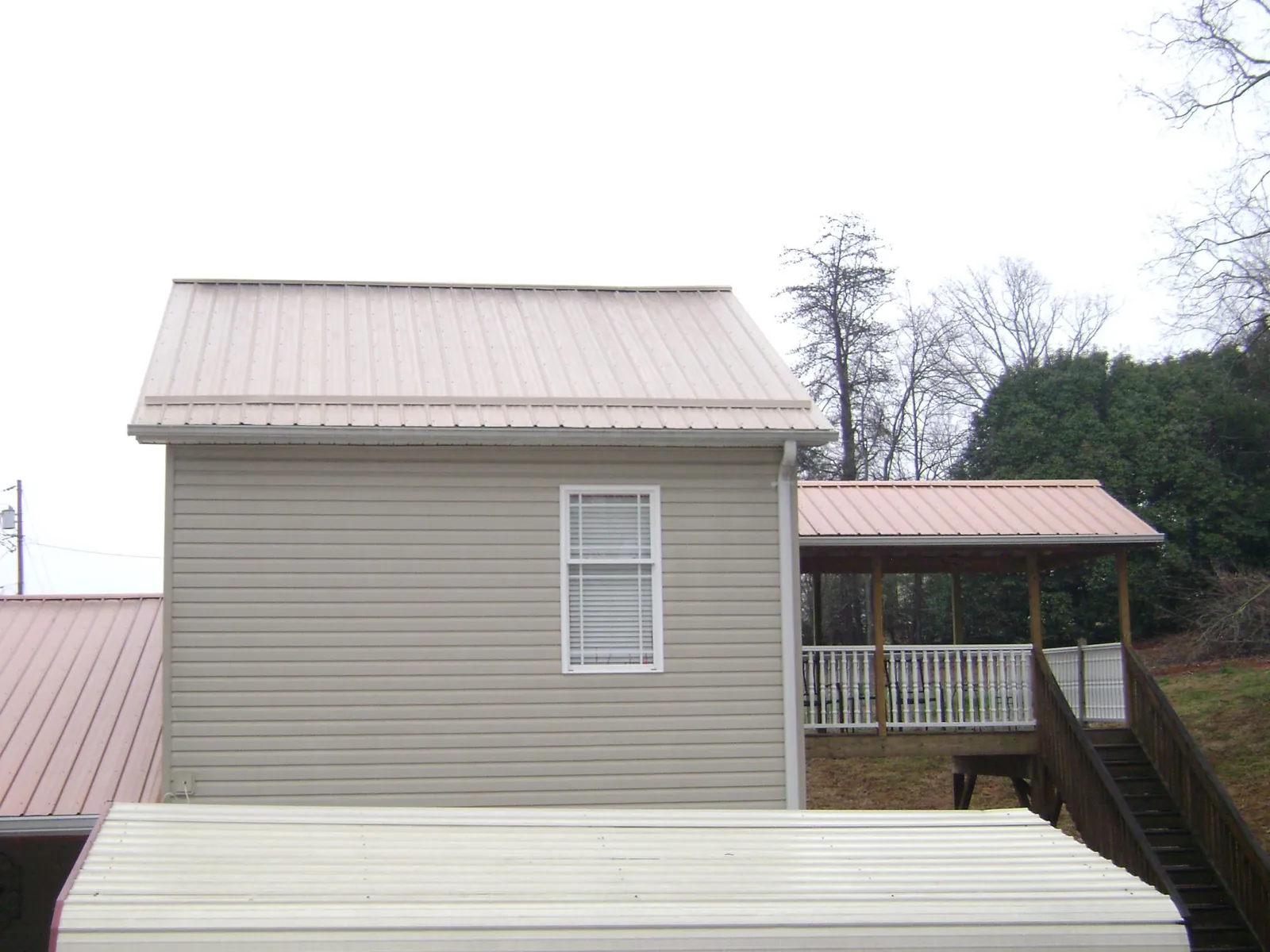 Tan metal roofs on a two story addition and attached porch, from a Roof Replacement job in Labadie