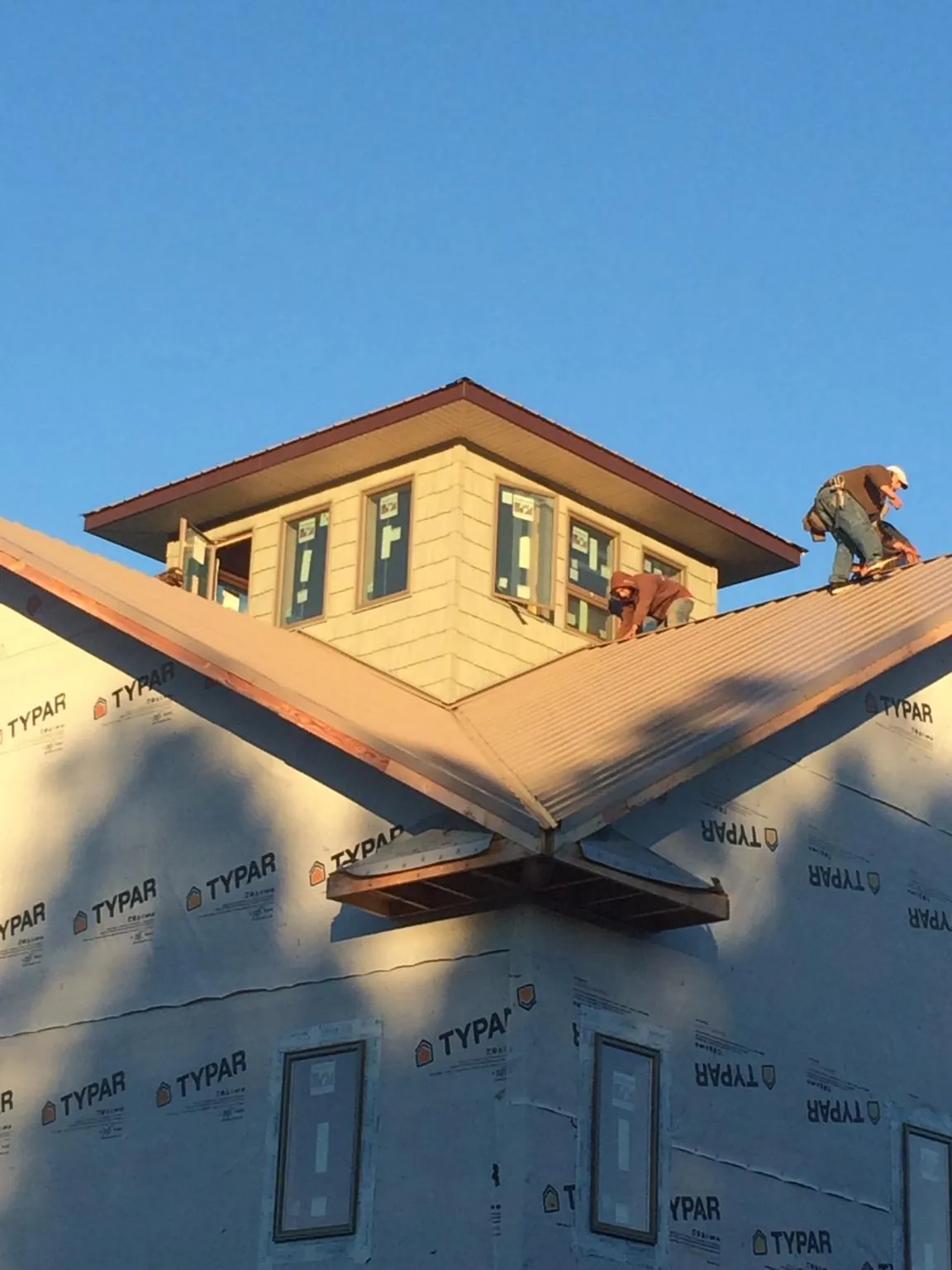 Roofers working around a rooftop cupola on a new metal roof at sunset in Labadie